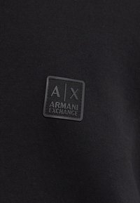 Čierny bavlnený odev s textúrovaným, obdĺžnikovým čiernym gumovým logom s označením "ARMANI EXCHANGE" a štýlovým dizajnom "A/X".