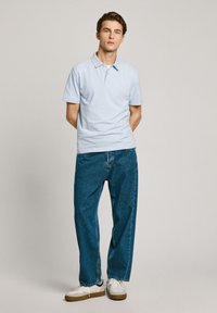 Světlomodré pruhované polo tričko s límečkem, spárované s volnými tmavomodrými denimovými džíny a bílými teniskami s hnědými akcenty.