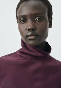 Burgundy turtleneck top made of silky fabric, featuring a high collar and smooth texture, with a simple and fitted design.