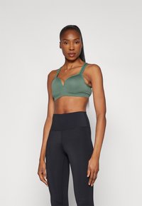 Grøn sports-bh med en dyb V-halsdesign og brede stropper, parret med højtaljede sorte leggings lavet af et glat, strækbart stof.