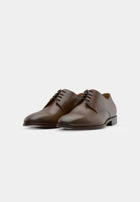 Scarpe in pelle marrone con punta arrotondata, texture liscia e design con lacci. Tacco basso e dettagli di cucitura minimalista.