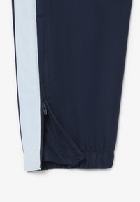 Marine sportieve broek met lichtblauwe zijpanelen, voorzien van een ritszak en een elastische tailleband, gemaakt van textuurstof die ademend is.
