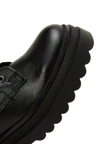 Czarne skórzane buty z zaokrąglonym czubkiem, teksturowaną cholewką i grubą, ząbkowaną podeszwą. Oczka i sznurowadła widoczne w górnej części.