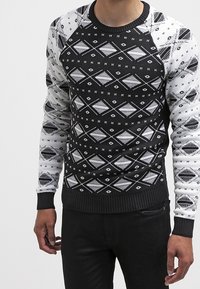 Pull à motifs noirs et blancs avec des designs géométriques, manches raglan, encolure et poignets côtelés, fabriqué en tissu tricoté.