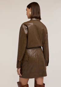Camicia in finta pelle marrone con maniche lunghe e polsini con bottoni, abbinata a una gonna alta in vita con tasche laterali.