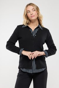 Cardigan nero con scollatura a V e chiusura con bottoni, indossato sopra una camicia a righe blu e bianche. Tessuto morbido, design aderente.