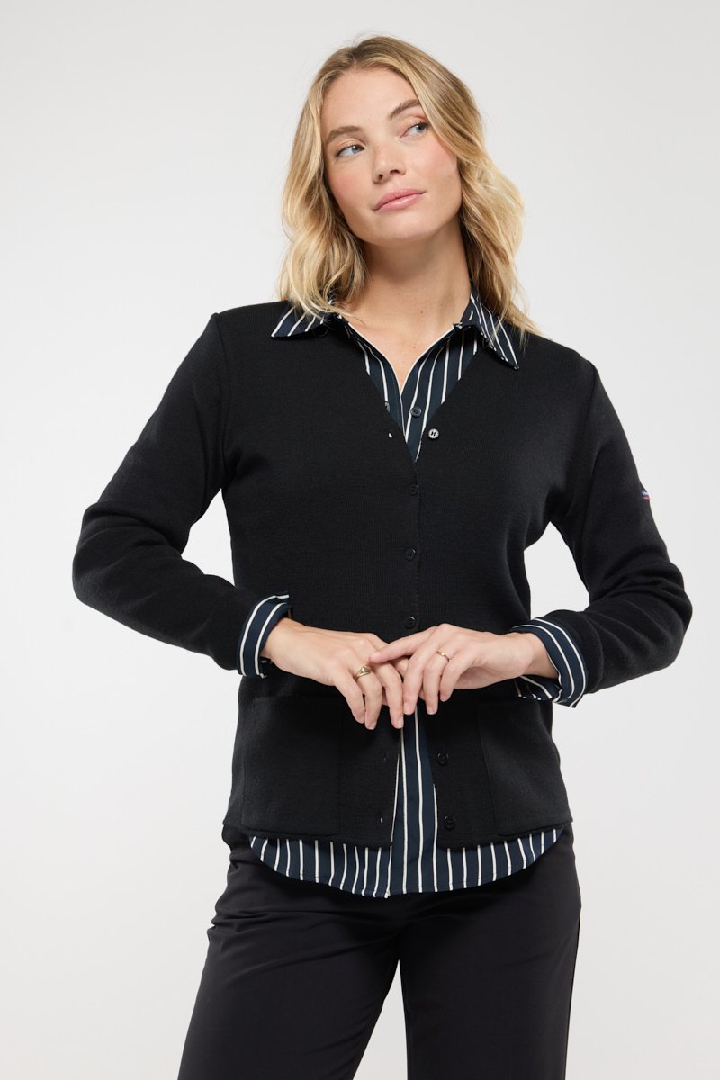 Cardigan nero con scollatura a V e chiusura con bottoni, indossato sopra una camicia a righe blu e bianche. Tessuto morbido, design aderente.