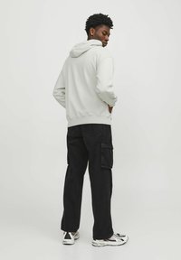 Lys grå hættetrøje med snoretræk i hætten, parret med sorte cargo bukser. Sættet har en afslappet pasform og tekstureret stof. Casual sneakers fuldender looket.