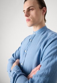 Lichtblauw, knoopsluiting shirt met een staande kraag, gemaakt van een gestructureerde stof en lange mouwen, weergegeven in een close-up view.