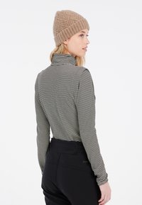 Schwarz-weiß gestreifter Langarmoberteil mit hohem Kragen, kombiniert mit schwarzen Hosen; Modell trägt eine sandfarbene strukturierte Strickmütze.