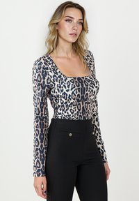 Beżowa bluzka z długim rękawem w panterkę, z kwadratowym dekoltem, w kolorach beżowym, czarnym i granatowym, zestawiona z czarnymi spodniami o wysokim stanie z guzikami.