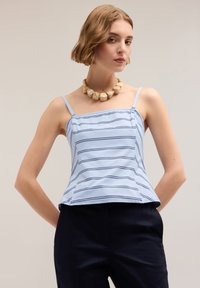 Camisola azzurro chiaro con righe orizzontali blu navy, spalline sottili e orlo svasato; indossata con pantaloni scuri, accompagnata da una collana beige voluminosa.