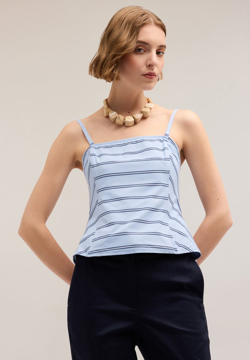 Camisola azzurro chiaro con righe orizzontali blu navy, spalline sottili e orlo svasato; indossata con pantaloni scuri, accompagnata da una collana beige voluminosa.