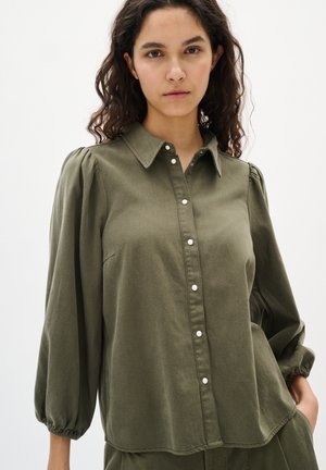 Chemise olive verte à boutonnage sur le devant en tissu doux, dotée d'un col, de manches bouffantes et de fermetures à boutons blancs sur le devant.