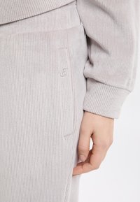 Lichtbeige ribgebreide joggingbroek met een geborduurd logo, voorzien van een zijzak en een zachte textuur.