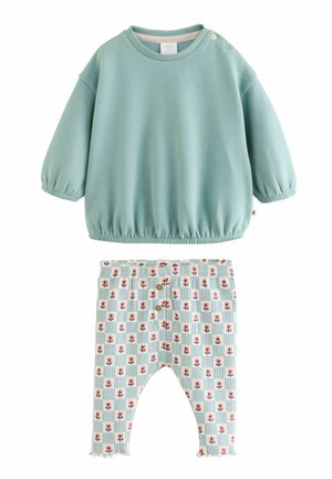 Blød grøn langærmet babybluse med elastiske manchetter og kant, kombineret med hvide leggings med blåt tern- og lille orange blomsterprint.