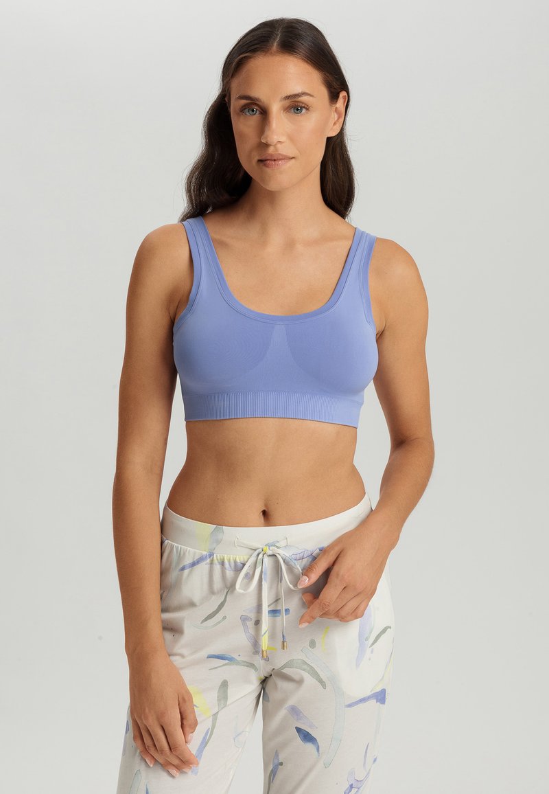 Helllila Sport-BH mit Rundhalsausschnitt und breiten Trägern, aus strukturiertem Stoff und nahtlosem Design. Kombiniert mit gemusterten hellen Hosen.