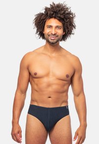 Slip da bagno a righe blu navy con copertura moderata, realizzati in tessuto liscio, con una fascia elastica in vita e dettagli di cucitura discreti.