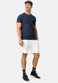 Marineblå strukturert t-skjorte med korte ermer og brystlomme, sammen med hvite shorts. Sorte sko og sokker fullfører antrekket.