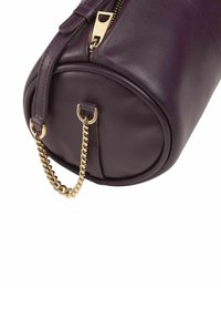 Bolso cilíndrico de cuero morado con un acento de cadena dorada, cierre de cremallera y asa superior. Textura suave, diseño minimalista.