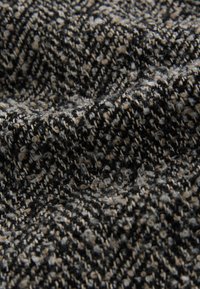 Czarna i beżowa tkanina o teksturze z subtelnym wzorem jodełki, zróżnicowaną grubością nici oraz miękką, lekko meszgowatą powierzchnią.