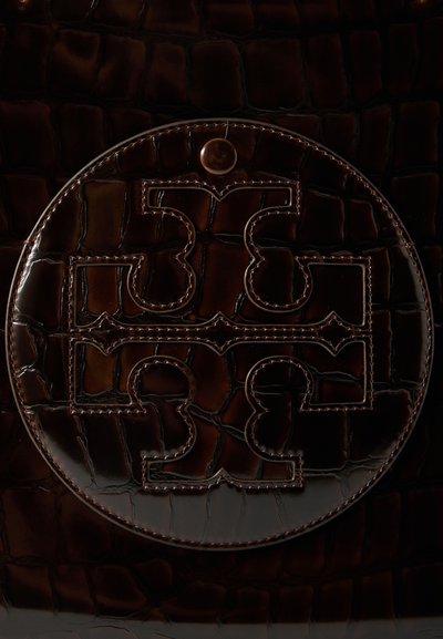 Ciemnobrązowa błyszcząca skóra z wytłoczonym i przeszytym okrągłym emblematem, na którym widnieje symetryczny wzór przypominający puzzle.