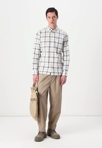 Πουκάμισο καρό από βαμβάκι σε λευκό, μπλε και μπεζ, με γιακά που κουμπώνει. Συνδυασμένο με μπεζ φαρδιά παντελόνια και κρατώντας μία μπεζ τσάντα. Ανοιχτό καφέ παπούτσια.