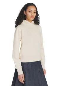 Felpa color crema in morbido tessuto con orlo e polsini a costine, caratterizzata da un delicato logo ricamato sul petto, abbinata a una gonna di jeans.