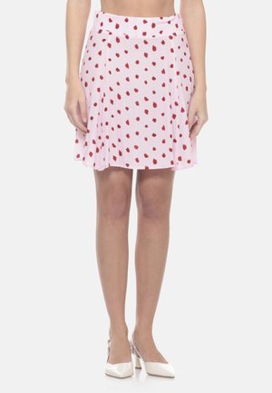 Donna che indossa una gonna a ruota rosa chiaro con pois floreali rossi e décolleté slingback bianche con punta appuntita, in piedi davanti a uno sfondo bianco.