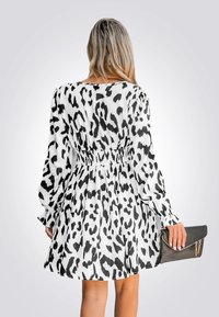 Abito a maniche corte con stampa animale bianca e nera, vita arricciata e gonna fluida. Borsa a tracolla nera tenuta nella mano destra.
