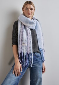 Sciarpa blu chiaro con strisce viola, bordi frangiati e una finitura testurizzata. Etichetta attaccata che riporta "COLORFUL" in blu navy. Indossata sopra una maglia scura.