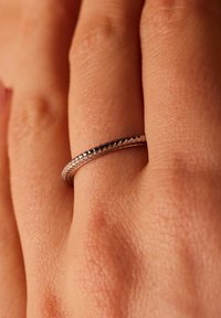 Verzilveren ring met een gladde band, voorzien van een gestructureerde rand. De ring ligt op een hand tegen een neutrale achtergrond.