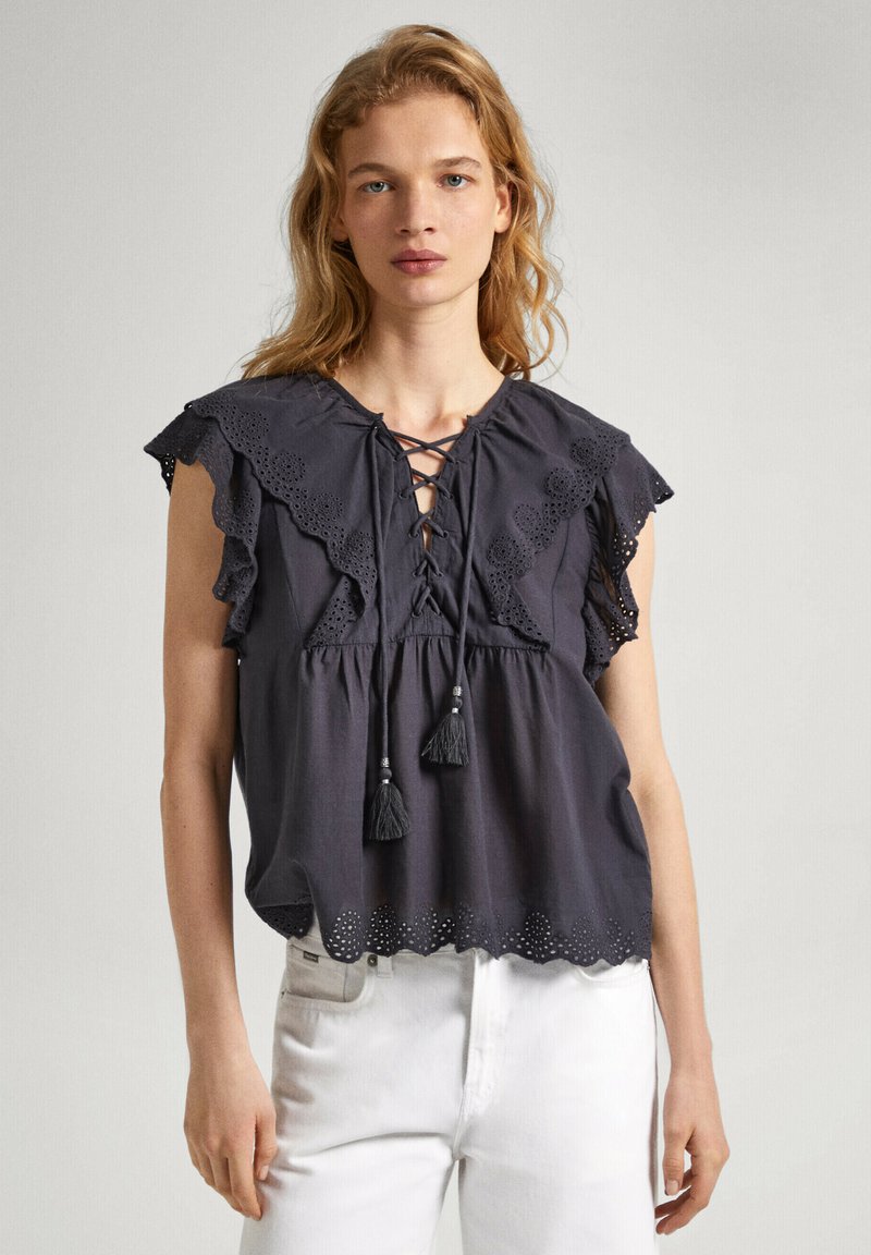 Blusa grigia scura con maniche a volant, scollatura a lacci e dettagli con nappine. Presenta un particolare in broderie anglaise all'orlo per aggiungere texture e design.