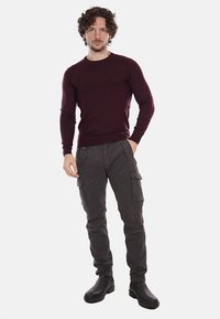 Suéter burdeos de cuello redondo, silueta ajustada; pantalones cargo grises con múltiples bolsillos; botas negras hasta el tobillo; textura suave; diseño casual.