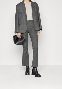 Donna che indossa un completo in zigzag grigio con una cintura larga, top beige, stivaletti neri con tacco e tiene una pochette nera con zip.