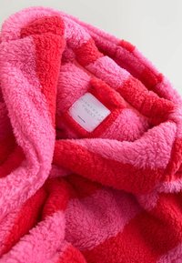 Fuzzy blanket in red and pink stripes, featuring a soft texture and a label reading "NIGHTWEAR by NEXT."