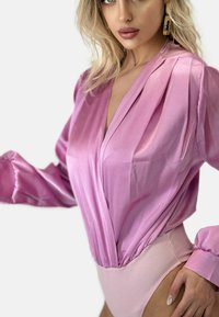 Body in misto seta di colore rosa chiaro con maniche lunghe a sbuffo, scollatura a V profonda e dettagli arricciati in vita per una forma e una texture fluida.