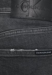 Svarta denimjeans med en subtil textur, med en läderlogotyp och stickningsdetaljer. Midjebandet har en märkeslabel.