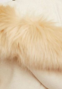 Tejido color crema con un acento de piel de pelaje ligero color beige; textura suave con un acabado liso. El pelaje es prominente a lo largo de un borde.