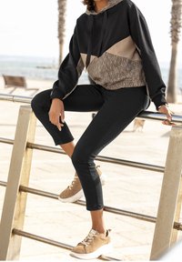 Black and beige color-blocked hoodie with a patterned design, paired with black tapered pants and tan sneakers with white soles.