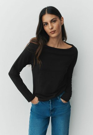 Sort langærmet top med bådudskæring, parret med højtaljede blå denimjeans. Glat stoffinish, afslappet pasform, minimalistisk design.