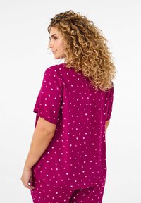 Magenta kortärmad topp med vita hjärttryck, med en avslappnad passform och mjuk textur, bärs med matchande underdel.