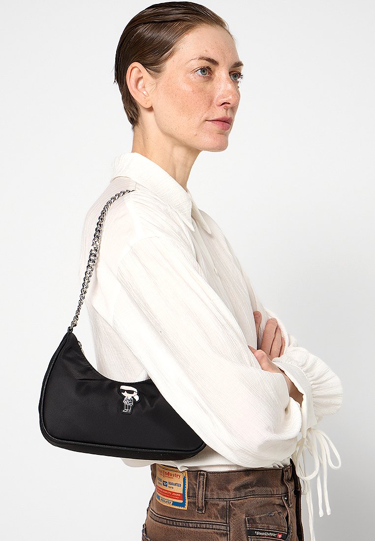 Sac à bandoulière noir en nylon avec une forme courbée, une chaîne argentée, et un petit ornement graphique à l'avant. Texture lisse et design minimal.