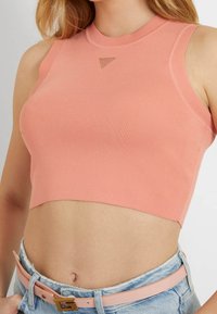 Geripptes Crop-Top in weichem Koralle mit hohem Ausschnitt und sportlichem, ärmellosem Design, kombiniert mit ausgewaschenen, hoch taillierten Shorts in Blau und einem pinkfarbenen Gürtel.