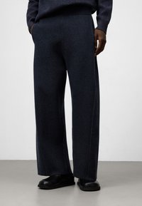 Mörkblå vida byxor i en strukturerad tygtyp, med hög midja och sidofickor, som är ihop med svarta slip-on skor.