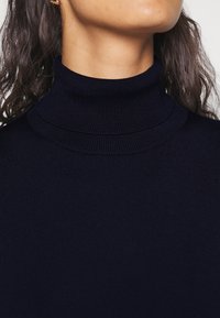 Laivastonsininen ribbineuleinen poolopaita, jossa on istuva kaulus ja sileä pinta. Lähikuva korostaa mallin ja materiaalin yksityiskohtia.