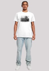 White t-shirt featuring a graphic print of the Batmobile in black and grey, paired with light blue jeans and white sneakers.