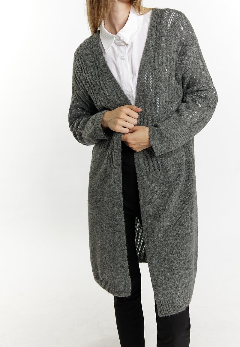 Cardigan long à ouverture frontale en matériau tricoté gris foncé, présentant une texture côtelée et des motifs délicats le long des manches.