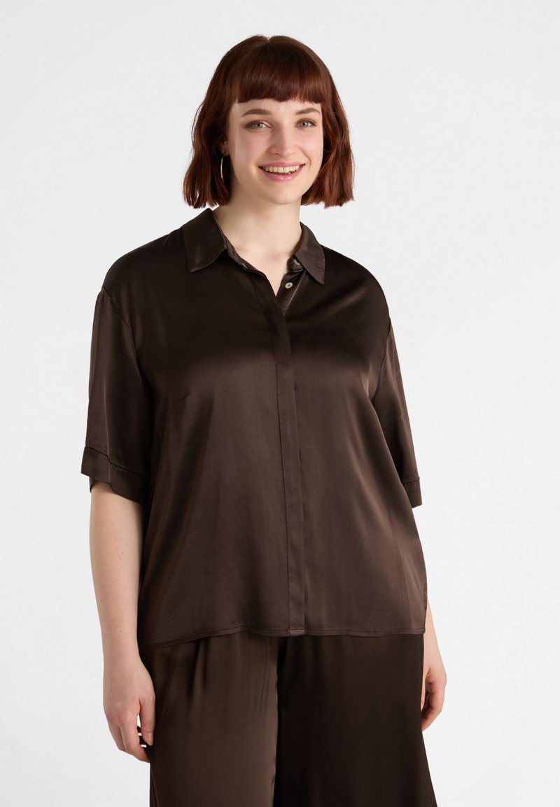Camicia corta a maniche corte in satin marrone con colletto e chiusura frontale con bottoni. Texture liscia e vestibilità comoda.