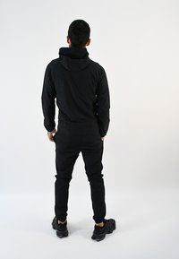 Conjunto atlético negro que consiste en un sudadera con capucha y pantalones ajustados, fabricados de un tejido suave y elástico sin patrones visibles.